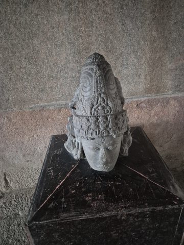A detached head wears a pointed, intricately ornamented headdress. The broken lower edge and the plinth beneath it remain visible.