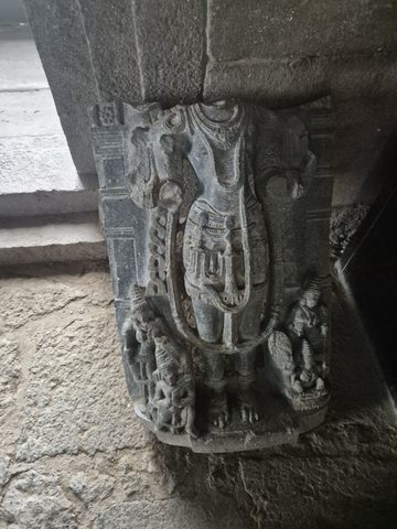 A standing figure survives below a broken neck. A long garland runs down the body, with smaller figures beside the legs.