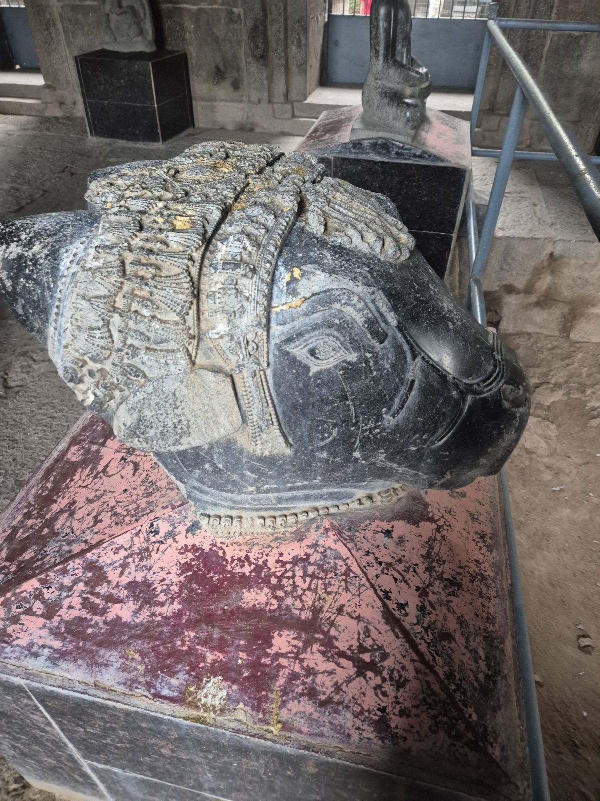 An animal head is seen from the side, with a prominent eye and bands of ornament across its upper surface. Cracks and pale surface deposits are visible.