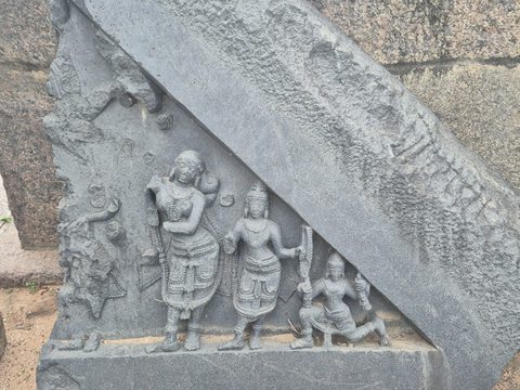 Standing and seated figures occupy a triangular field beneath a heavy diagonal border. Part of the carving is obscured by an overlapping stone.