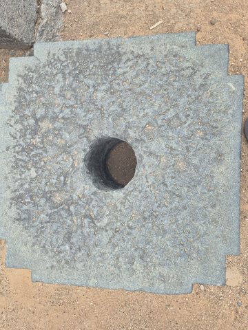 A square stone slab has stepped corners and a circular opening near its centre. Its original use is not established.