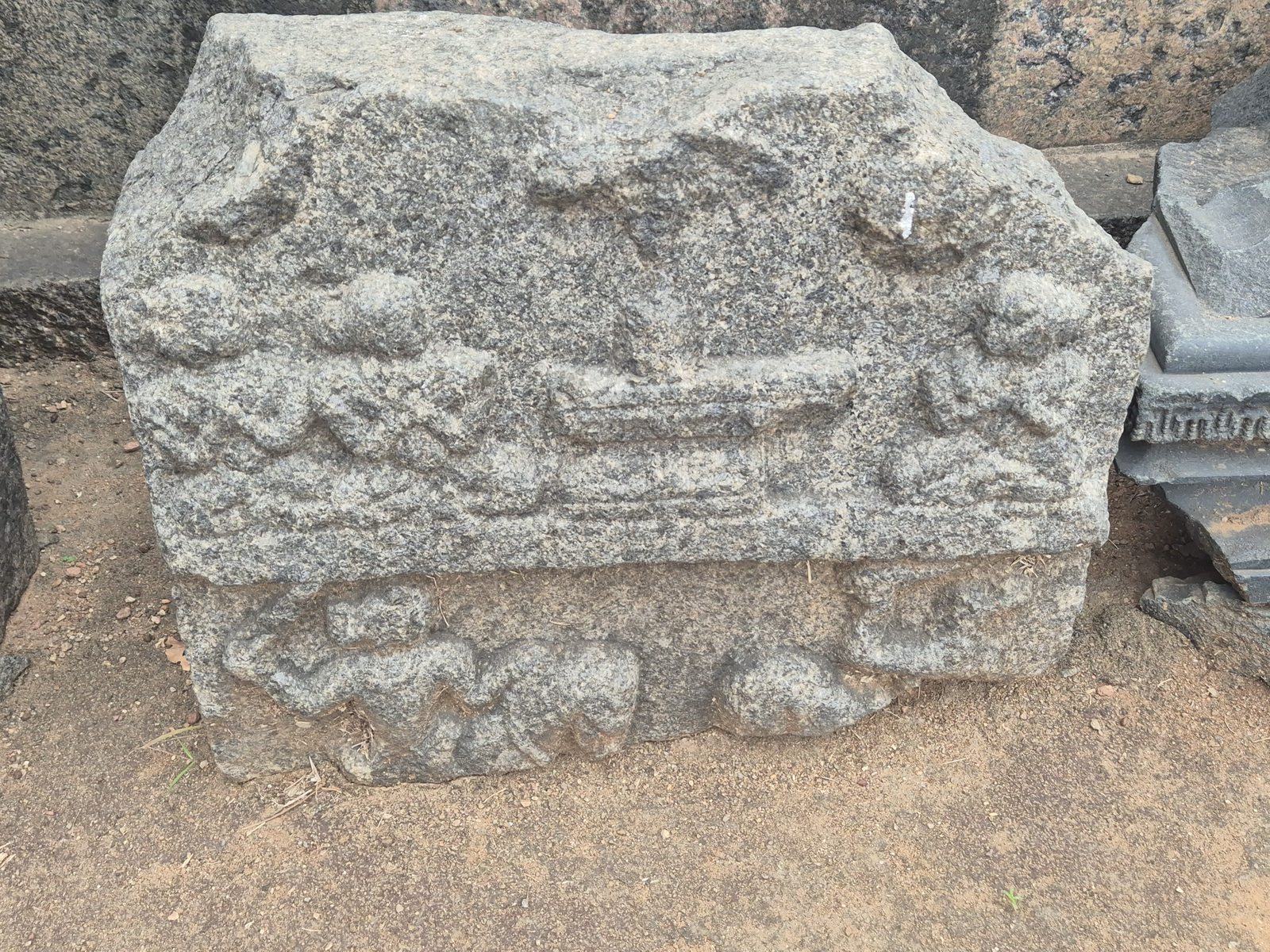 Rounded forms and horizontal mouldings remain visible across a worn stone block. The upper edge is irregular and broken.