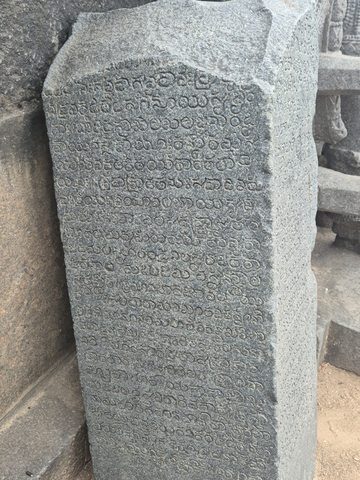 Closely spaced characters run down a narrow upright stone. Wear and the angle of the photograph limit the reading of individual marks.