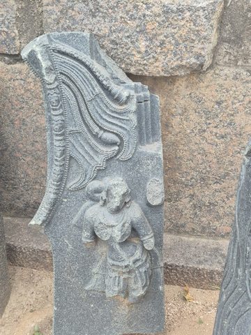 Layered, sweeping carved bands curve above a small figure. The fragment narrows upward and ends at a broken edge.
