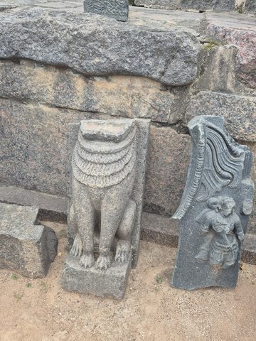 Two separate carved fragments stand beside one another: a surviving lower body and a tapered piece with curved bands. Their original relationship is not known.