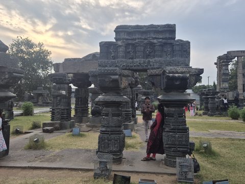 Short, richly carved columns support stacked horizontal pieces. Visitors and other assemblies remain visible in the surrounding grounds.