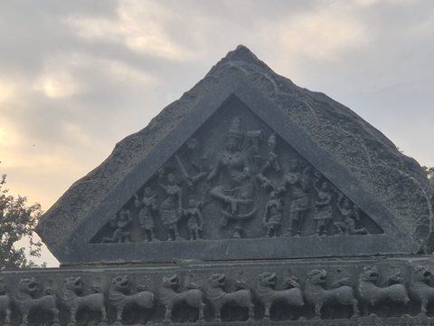 Figures fill a triangular panel above a row of animals. Two photographs show the panel at different distances against the evening sky.