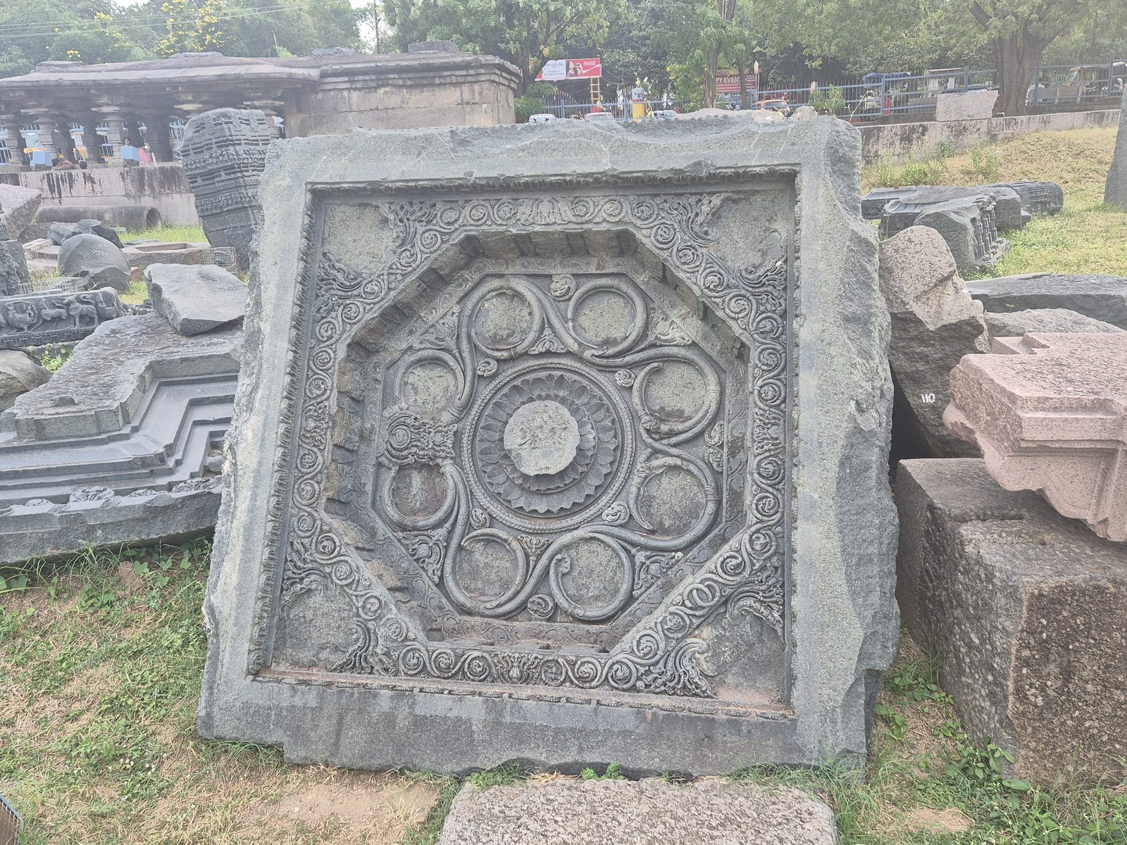 A ring of circular motifs surrounds a central disc inside an angular border. Scrolling ornament fills the outer corners of the square panel.