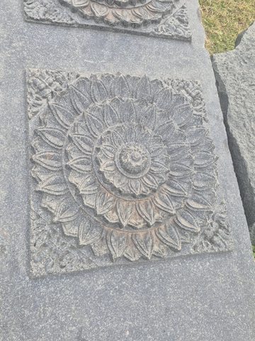 Concentric layers of pointed petals surround a small central face-like form. This photograph is a close view of a larger stone surface.