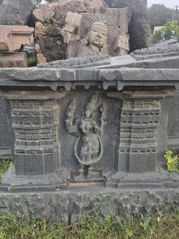 A small standing figure occupies a narrow framed recess between layered architectural forms. A separate carved head is visible behind the panel.