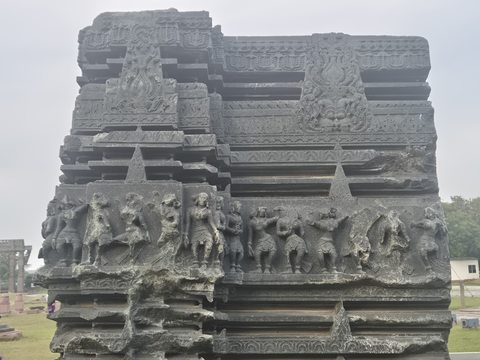 Animals and smaller figures run across the layered face of a tall fragment. A wider photograph includes the lower carved figure and the grass around it.