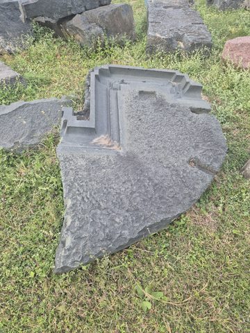 Parallel stepped mouldings meet at one corner of a thick slab. Much of the remaining edge is broken and irregular.