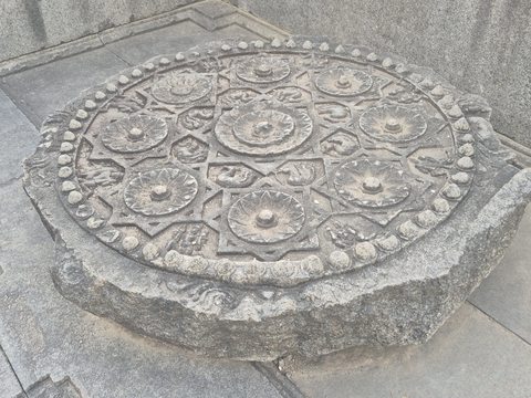 Small flower-like circles surround a central motif on a round disc. Its thick edge and the stone floor beneath are visible.