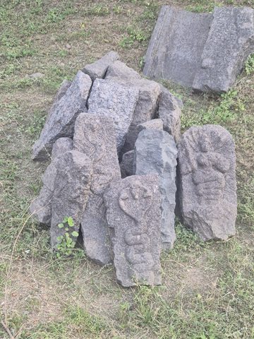 Small relief fragments lean against a group of larger stones. Their shapes and surviving figures vary; no reconstruction is proposed.