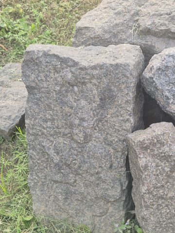 A faint standing form is visible on a weathered upright piece among larger stones. Surface loss makes the details difficult to distinguish.