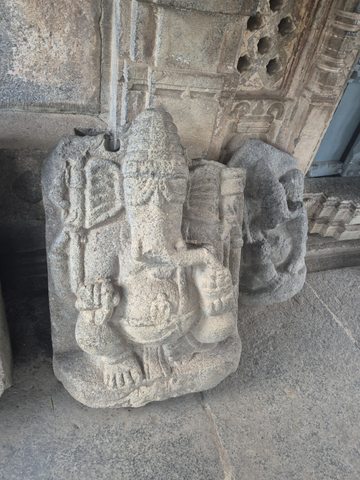 A seated figure has a long trunk, a tall headdress and several arms. The available view includes the worn backing slab and the carved doorway behind.