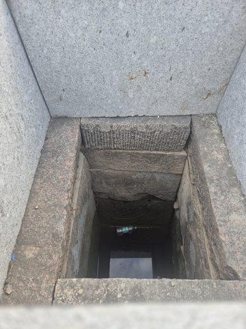 A downward view records a rectangular opening lined with stone. Dark space and some water or reflective surface are visible below; its original function is unverified.