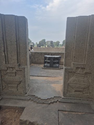 Carved vertical sides frame an open doorway leading into a stone enclosure. A low object stands beyond the threshold.