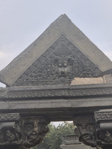 A triangular panel with scrolling ornament and a central face-like form sits above paired columns. A missing section interrupts the lower edge of the triangle.