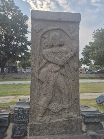 A figure stands within a tall rectangular panel beneath a curling border. The worn face and angled objects across the body are retained as photographed.