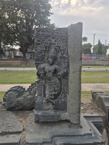 A standing figure survives beside dense scrolling ornament on an upright fragment. One edge is broadly broken and rough.