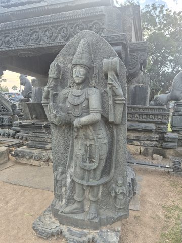 A crowned standing figure holds its arms around a tall upright form. Layered jewellery and garment details survive down to its feet.