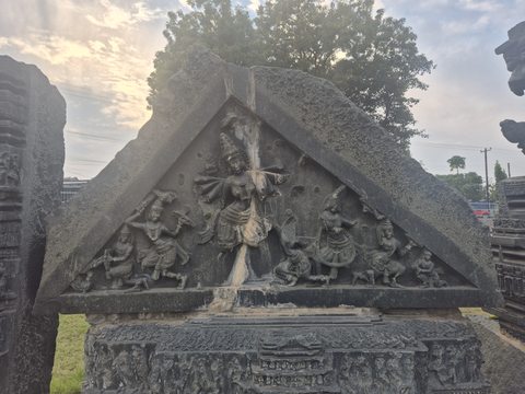 A central figure and smaller flanking figures fill a triangular panel. A second photograph records the horizontal carved pieces beneath it, without implying an original reconstruction.