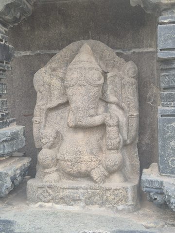 A seated elephant-headed figure occupies the space between carved stone supports. The wider photograph records the surrounding beams and platform; their original relationship is not established.